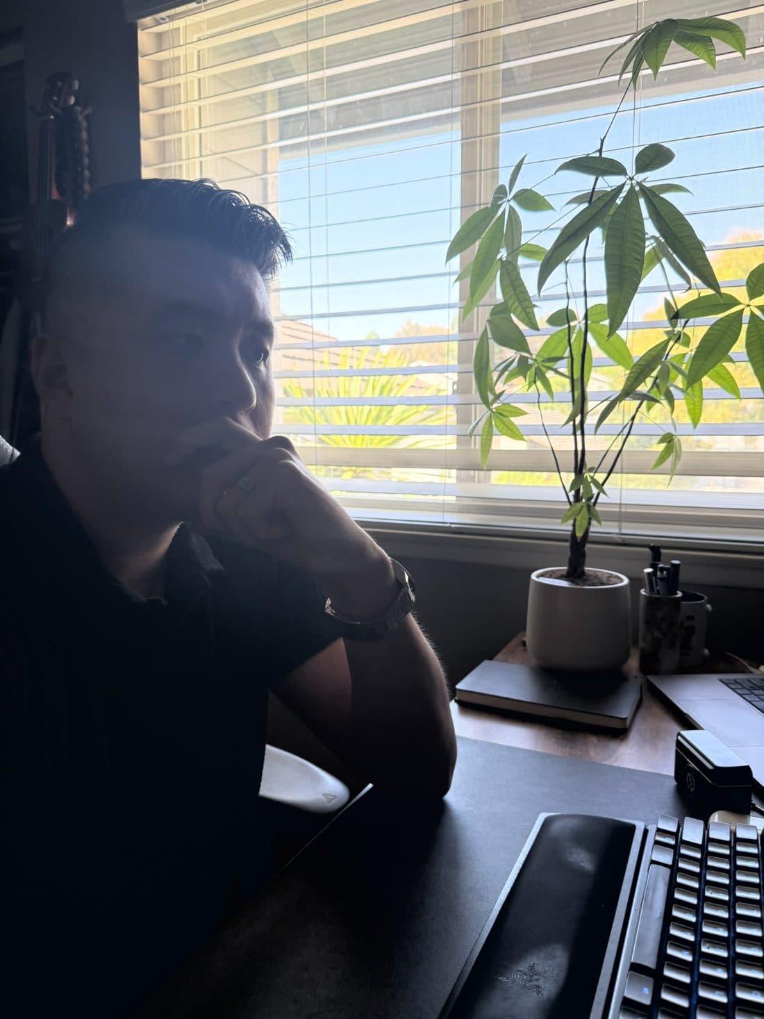 Lawrence sitting at his desk in hard window light, chin on his hand, looking away from the screen.